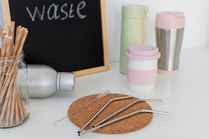 Reusable metal straws and eco-friendly cups on a table with a chalkboard displaying the word waste.