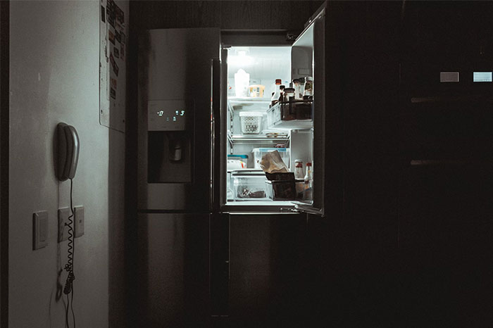 Open refrigerator in a dark kitchen, showing food containers and bottles inside, illustrating timestamped pictures concept.