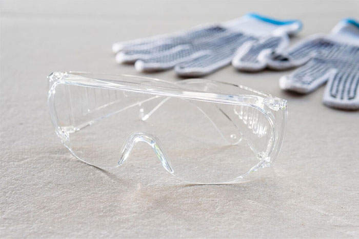 Clear protective safety glasses and work gloves on a surface symbolizing random things that saved people later.