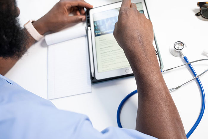 Person using a tablet to view timestamped pictures while sitting at a desk with a stethoscope nearby.