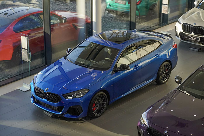 Blue BMW car displayed in a showroom with reflections capturing timestamped pictures of a rainy day outside.