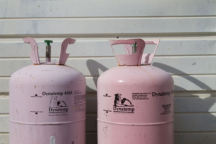 Two pink Dynatemp 410A refrigerant cylinders standing outdoors against a white wall, timestamped pictures concept.