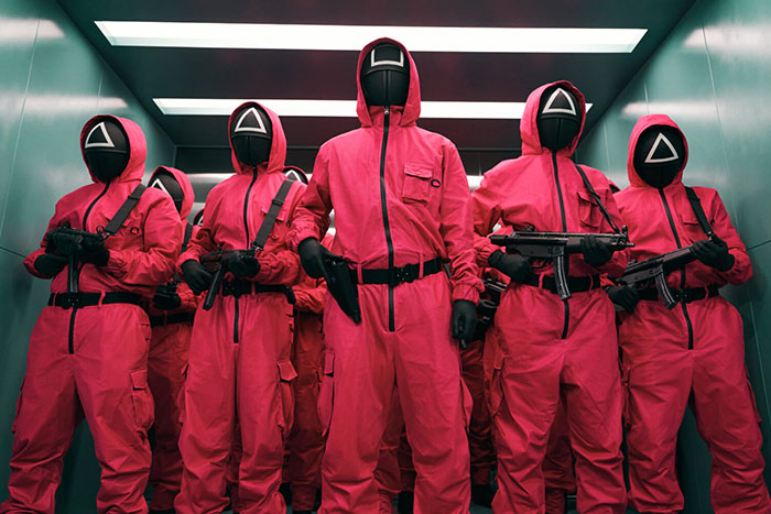 Guards in pink uniforms with geometric masks in a hallway, related to Squid Game 2 Easter eggs and clues.