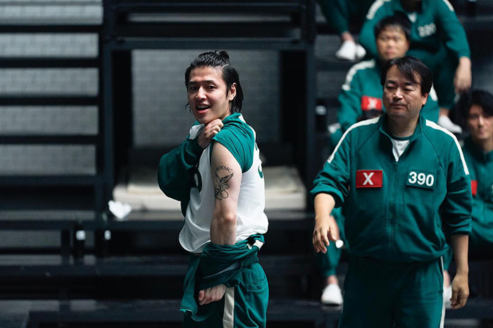 Two characters in green tracksuits reveal a tattooed Easter egg clue in Squid Game 2 scene.