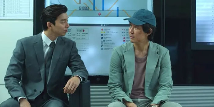 Two characters from a scene in Squid Game 2, possibly discussing hidden Easter eggs or clues, sitting together.