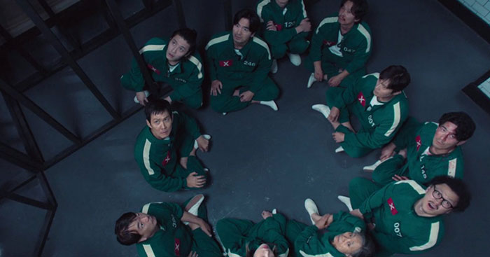 Contestants in green tracksuits sitting in a circle, potentially containing Easter eggs and clues for Squid Game season 2.