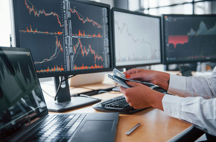 Person holding cash in front of monitors showing stock graphs, relating to UnitedHealth's $63 billion value loss. Person holding cash in front of monitors showing stock graphs, relating to UnitedHealth's $63 billion value loss.