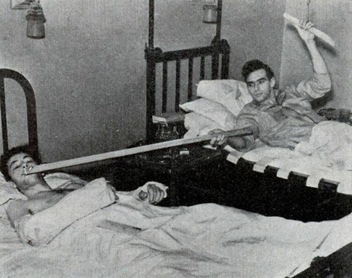 "Two men in hospital beds using a long stick for communication, illustrating a random fascinating fact."