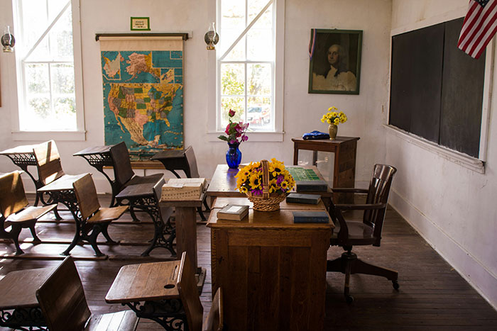 Vintage classroom with wooden desks, a map of North America, and flowers on a teacher's desk, evoking past educational settings. Vintage classroom with wooden desks, a map of North America, and flowers on a teacher's desk, evoking past educational settings.