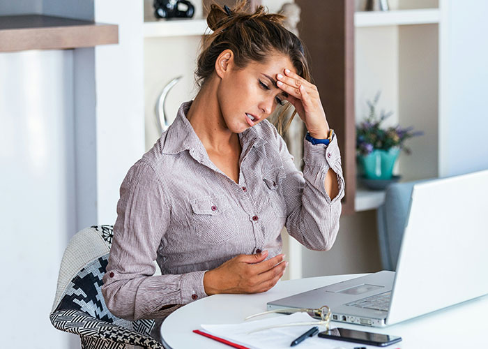 Woman in distress at a desk, possibly feeling unwell, related to vegetarian food theft at workplace.