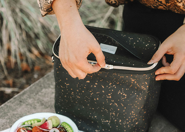 Person unzipping a black lunch bag beside a plate of vegetarian snacks.