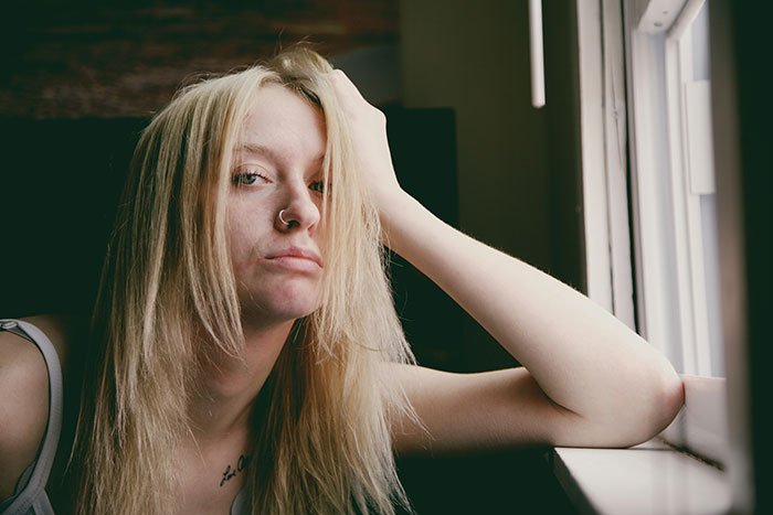 Woman with a nose ring, looking thoughtful by a window, representing dark secrets confessed while drunk.