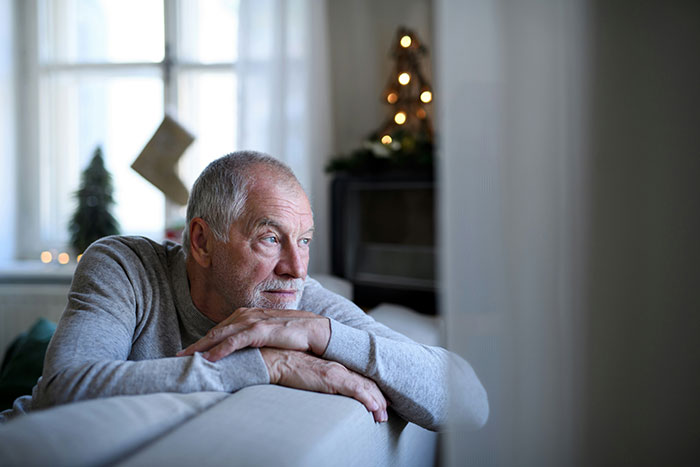 Elderly man in a thoughtful pose by the window, contemplating dark secrets.