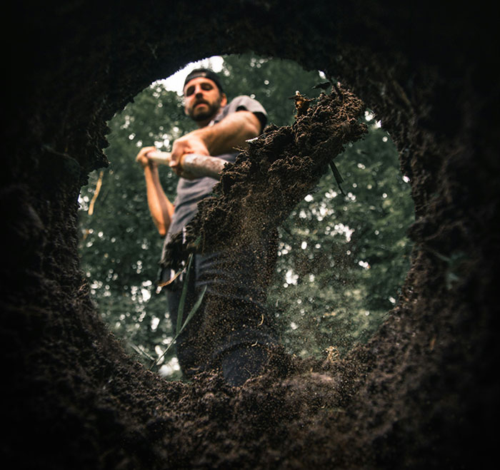 Man digging a hole in the forest, viewed from below, representing dark secrets.