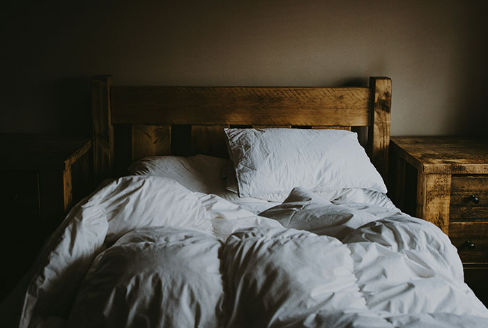 Cozy rustic wooden bed with white rumpled sheets, conveying warmth and secrecy.
