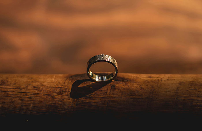 A single ring on a wooden surface with dramatic lighting, symbolizing dark secrets and personal confessions.