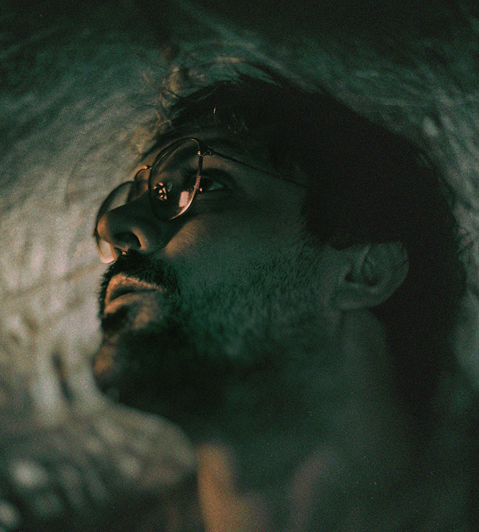 Man with glasses looking up in dim light, reflecting a mood of introspection and secrecy.