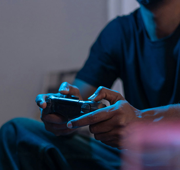 Person playing video game, holding a controller in a dimly lit room.