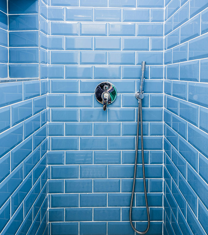 Shower with blue subway tiles and silver fixtures, featuring a simple and clean design.