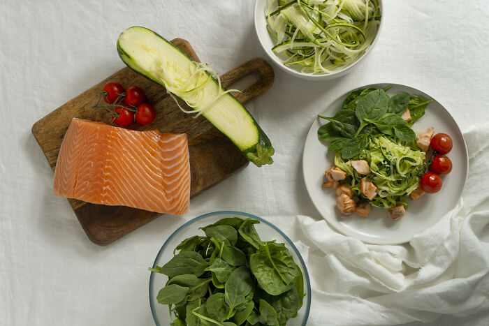 Fresh ingredients including salmon, zucchini, and spinach on a table, related to the biggest scam in human history.