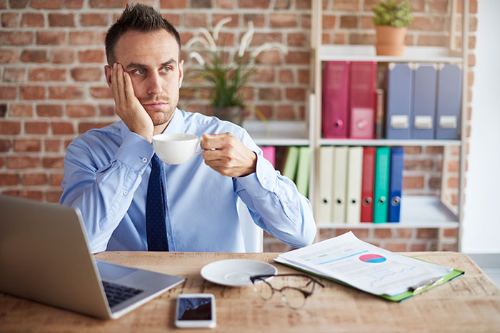 Man in an office looking thoughtful with coffee, open laptop, and documents on desk. Man in an office looking thoughtful with coffee, open laptop, and documents on desk.