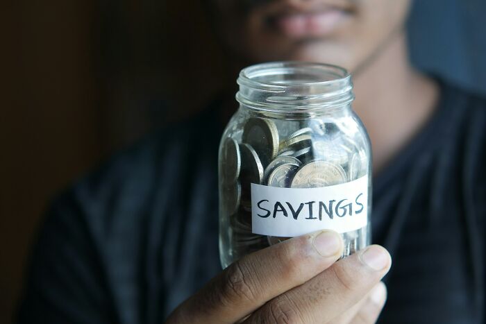 Person holding a jar labeled "savings," filled with coins, illustrating a strategy for reducing household budgets.