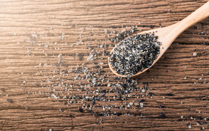 Wooden spoon with black salt granules on a rustic surface, highlighting toxic things and substances.