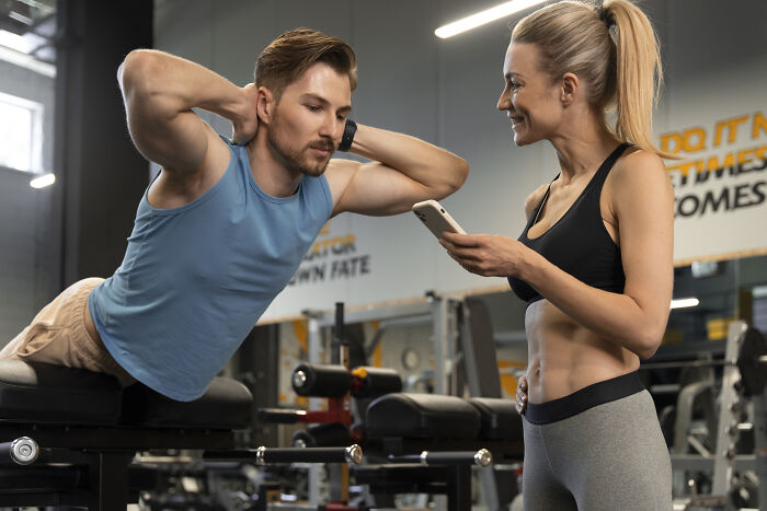Man exercising while woman holds phone, demonstrating affordable ways to make life easier in a gym setting.