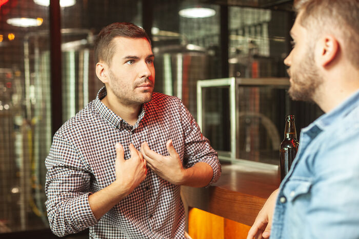 Two men at a bar, one gesturing while talking, possibly discussing maturity.