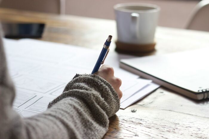 Person writing notes at a desk with a mug, highlighting outdated financial stereotypes.