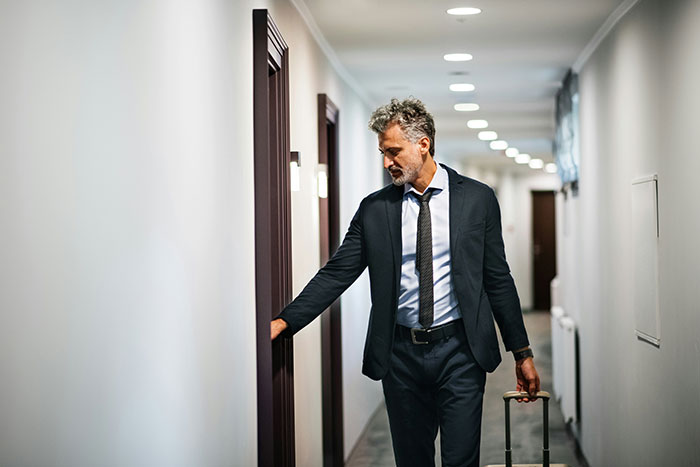 Man in a suit with luggage entering a hotel room, embodying hotel etiquette.