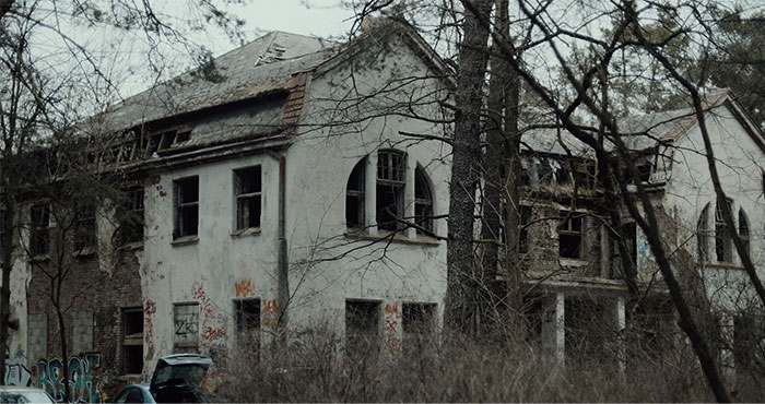Abandoned house linked to urban legends, with broken windows and graffiti, surrounded by trees.