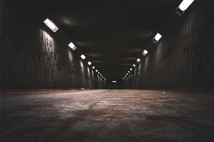 Dark, eerie urban legend setting in an empty underground tunnel with dim lights.