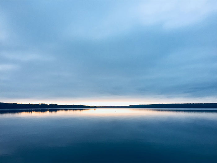 Calm lake at dusk with cloudy sky reflecting over the water, evoking mysterious urban legends.