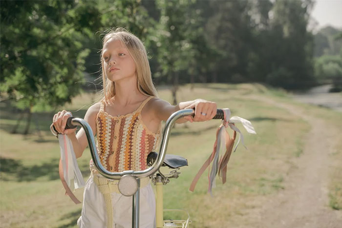 Young girl on a bike in a park setting, embodying urban legend themes with colorful streamers and serene atmosphere.