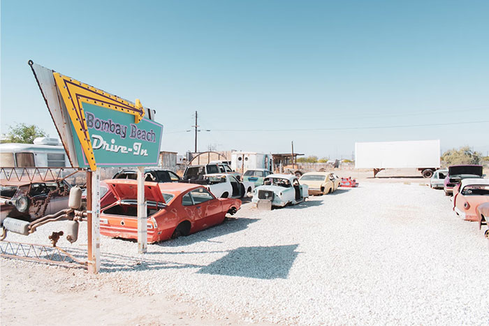 Bombay Beach Drive-In with abandoned cars under clear blue skies, highlighting urban legends.