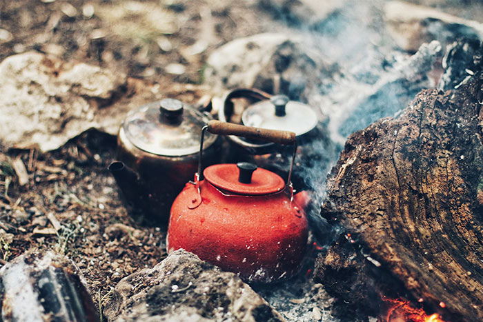 Red and silver kettles on a campfire in a forest setting, linked to urban legends.