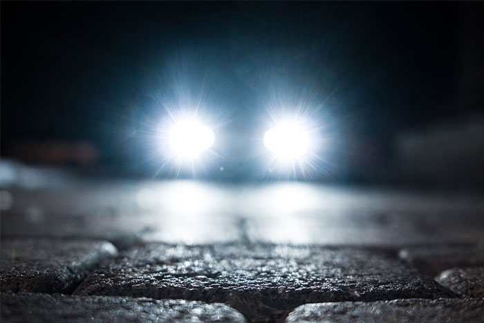 Car headlights shining on a cobblestone street, representing urban legends.