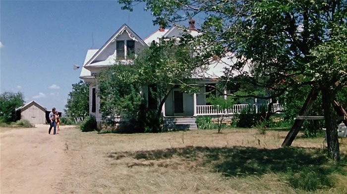 Rural house with large porch and tree, reminiscent of true urban legends, under a clear blue sky.
