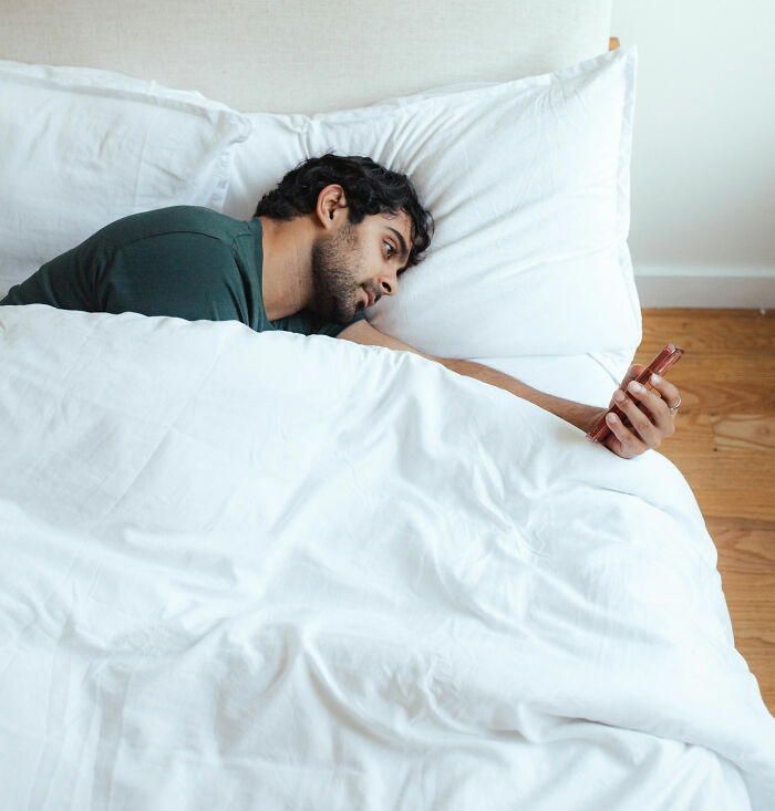 Man lying in bed, casually holding a smartphone, exhibiting non-s****l behavior that attracts women.