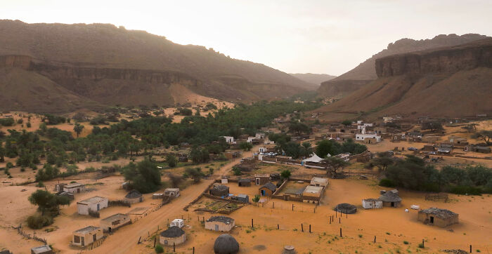A rural village scene with scattered huts and trees in a desert valley, illustrating challenges in the worst country ever visited.