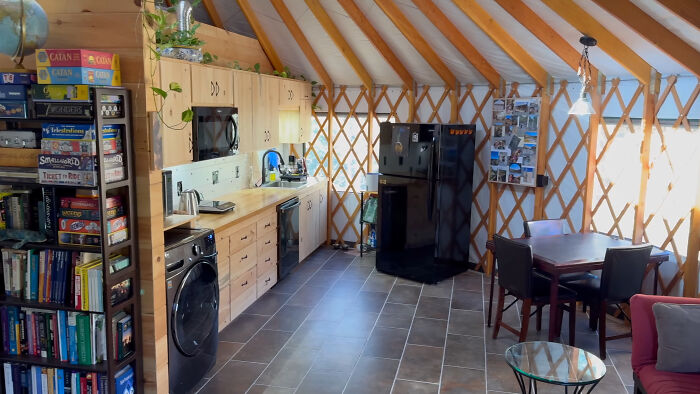 Interior of a self-built off-grid yurt featuring a kitchen, dining area, and bookshelf filled with games and books. Interior of a self-built off-grid yurt featuring a kitchen, dining area, and bookshelf filled with games and books.