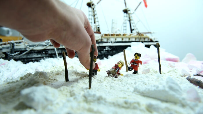 LEGO figures recreate the Imperial Trans-Antarctic Expedition on a snow-like surface with a ship in the background.