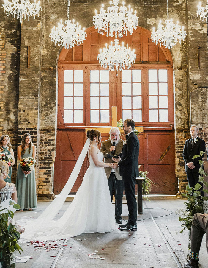 Bride and groom exchanging vows in a rustic venue, elegant chandeliers overhead, symbolizing a pivotal wedding moment. Bride and groom exchanging vows in a rustic venue, elegant chandeliers overhead, symbolizing a pivotal wedding moment.