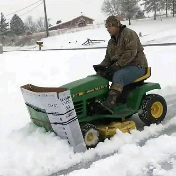 Man clearing snow with a lawn tractor and makeshift plow, showcasing weird and funny improvisation.