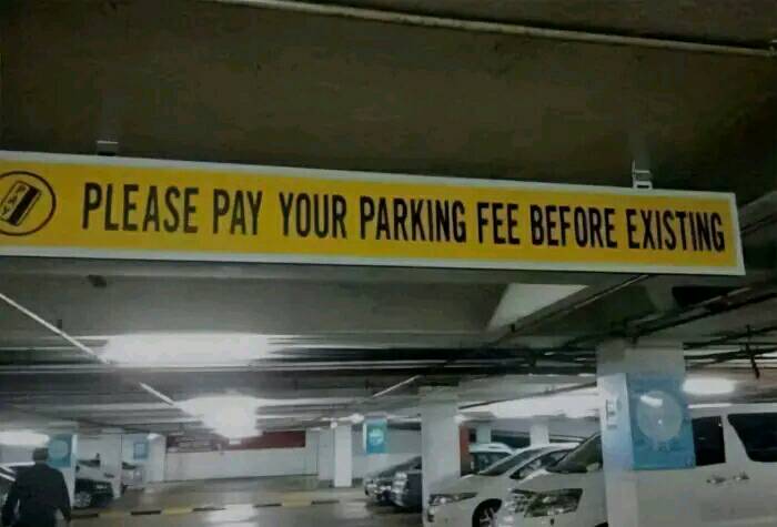 Bizarre parking sign with typo: "Please pay your parking fee before existing" in a dimly lit garage.