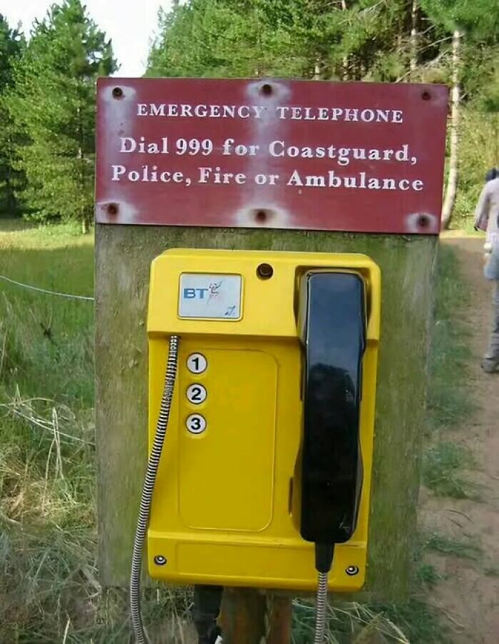 Bizarre emergency phone in the woods with a sign to dial 999 for services like coastguard and police.