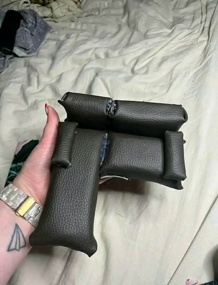 A hand holding a bizarre, pillow-shaped object resembling a toy gun on a bed.