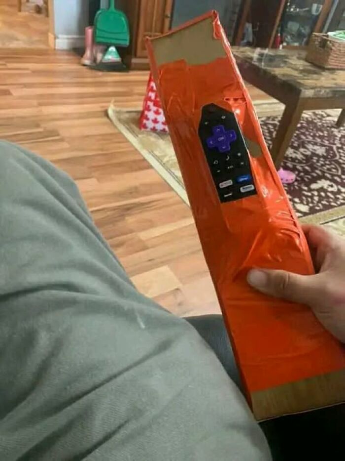 Remote taped to a long cardboard box, a bizarre and funny solution on a living room couch.