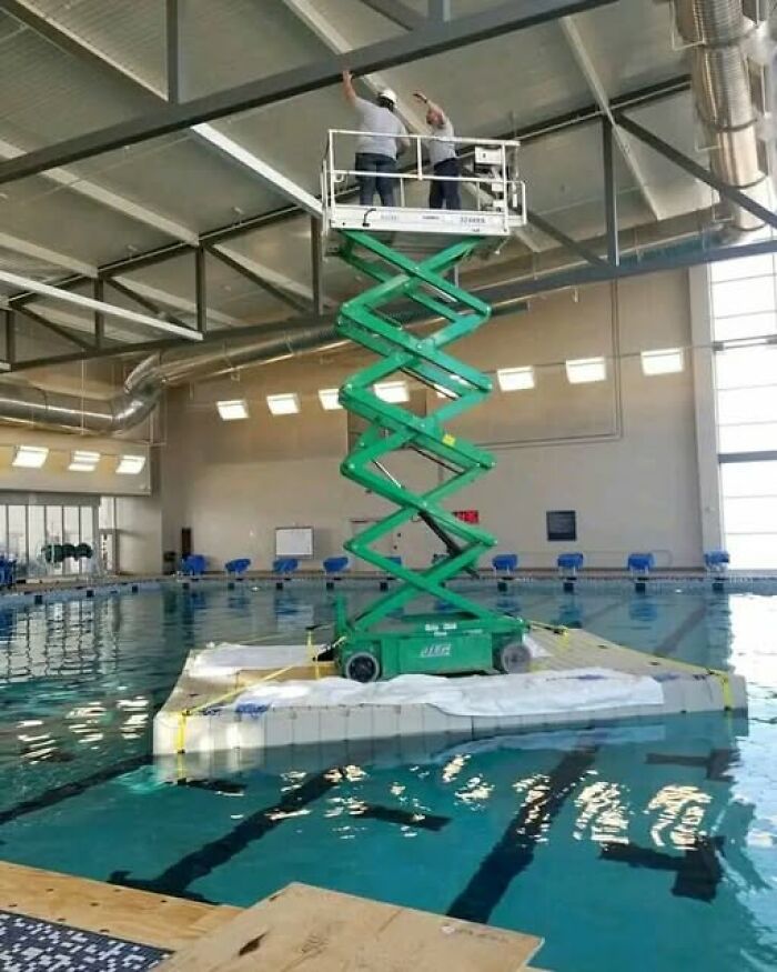 Scissor lift on a floating platform in a pool, capturing bizarre and funny scene.